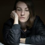 A woman in thought with a serious expression, indoors, in a low-light setting.